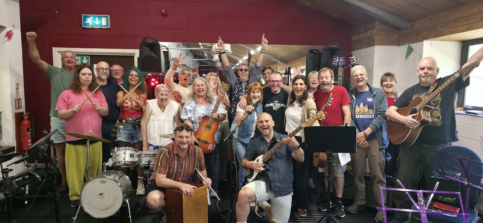A real group of people together in a hall, arms raised and playing instruments, at The Biggest Jam community music event