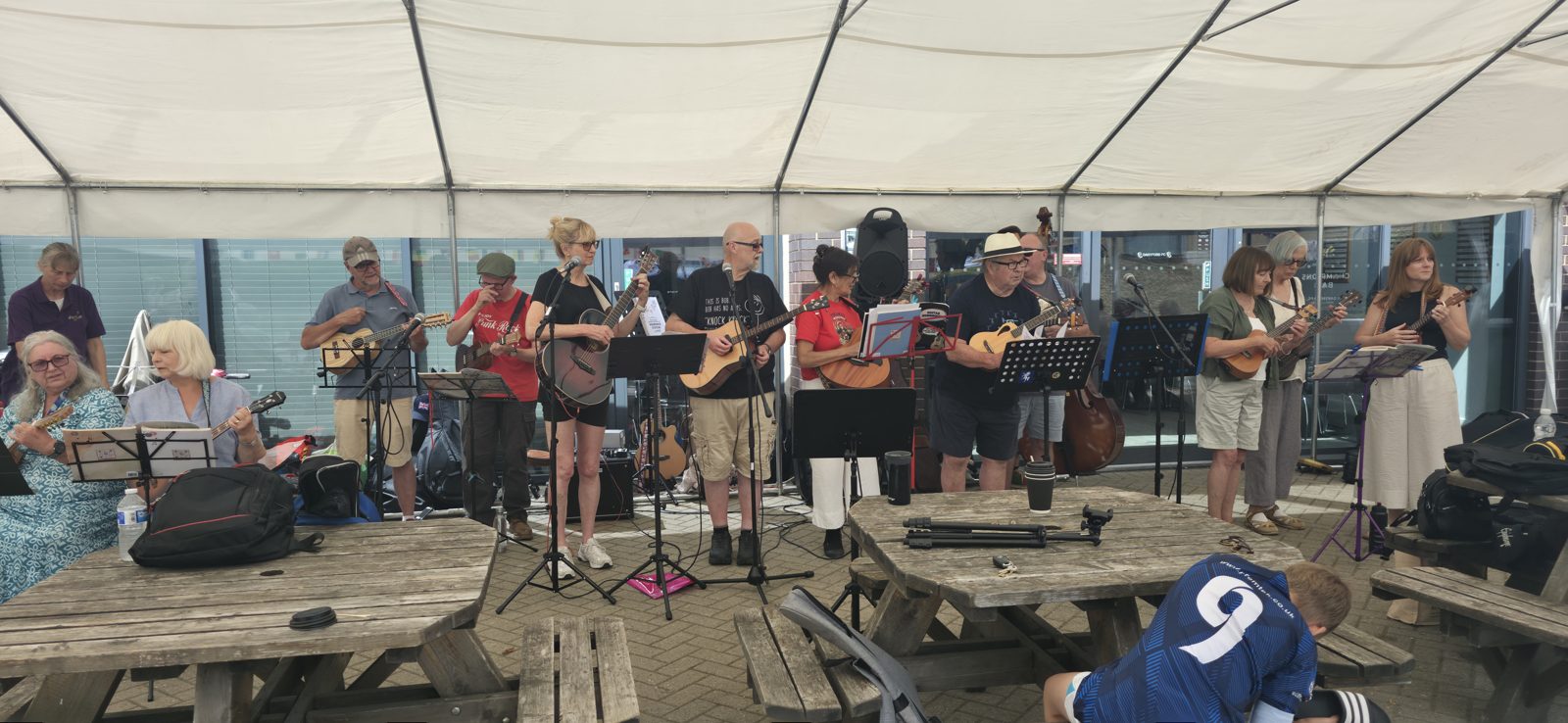 A community ukulele group performing under a marquee at Dartford Football Club