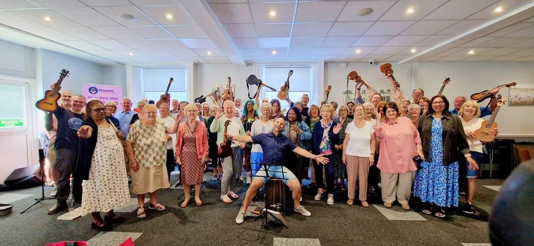 A large group of people holding ukuleles aloft together at the Masonic House, Dartford