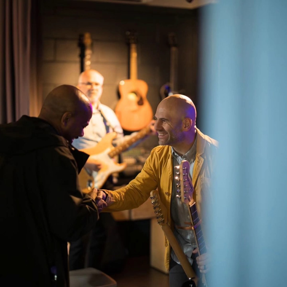 Barry de Jager smiling and shaking hands with a fellow musician before playing, guitars behind them