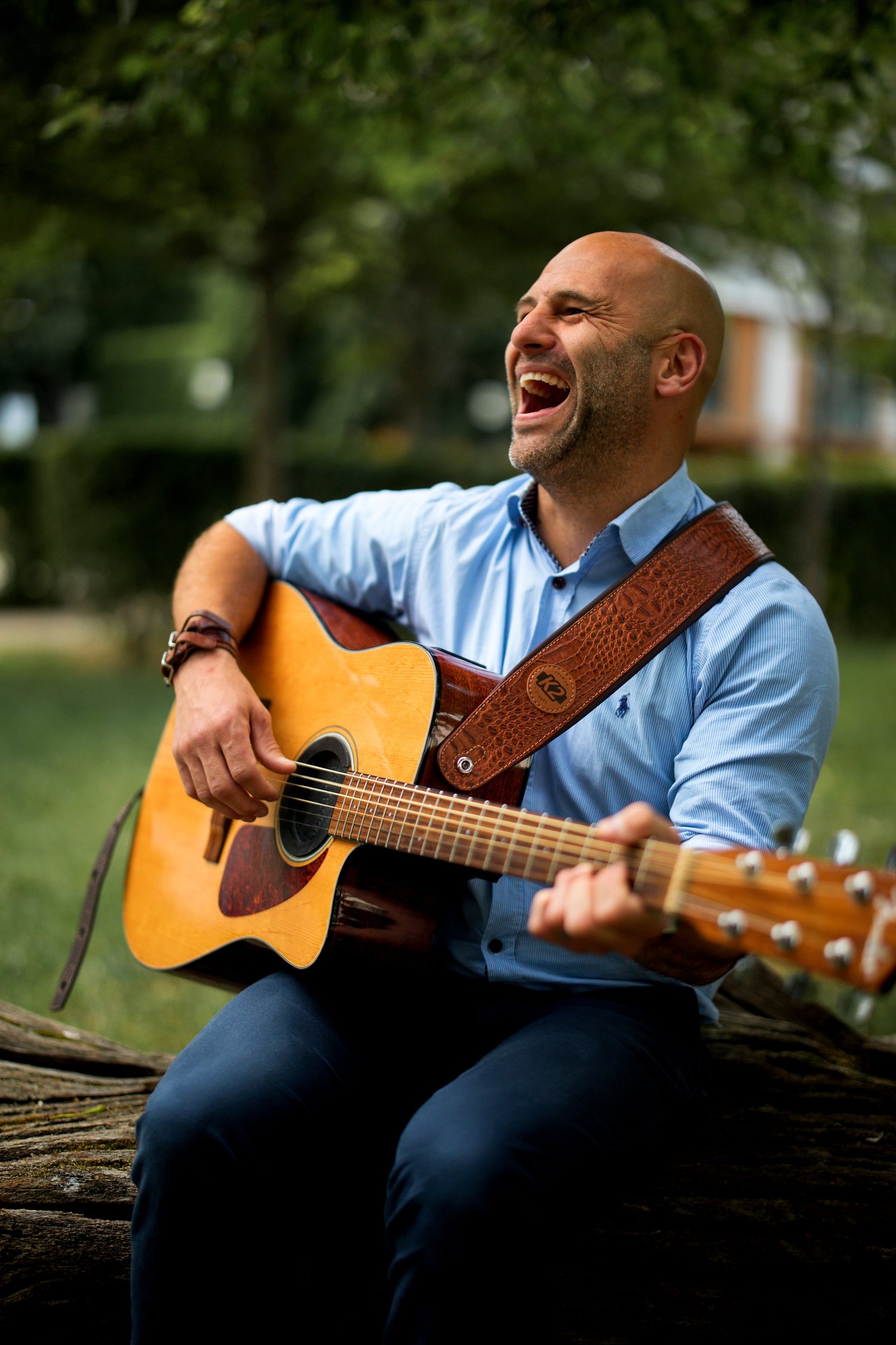 Barry de Jager playing an acoustic guitar and singing outdoors, mid-laugh
