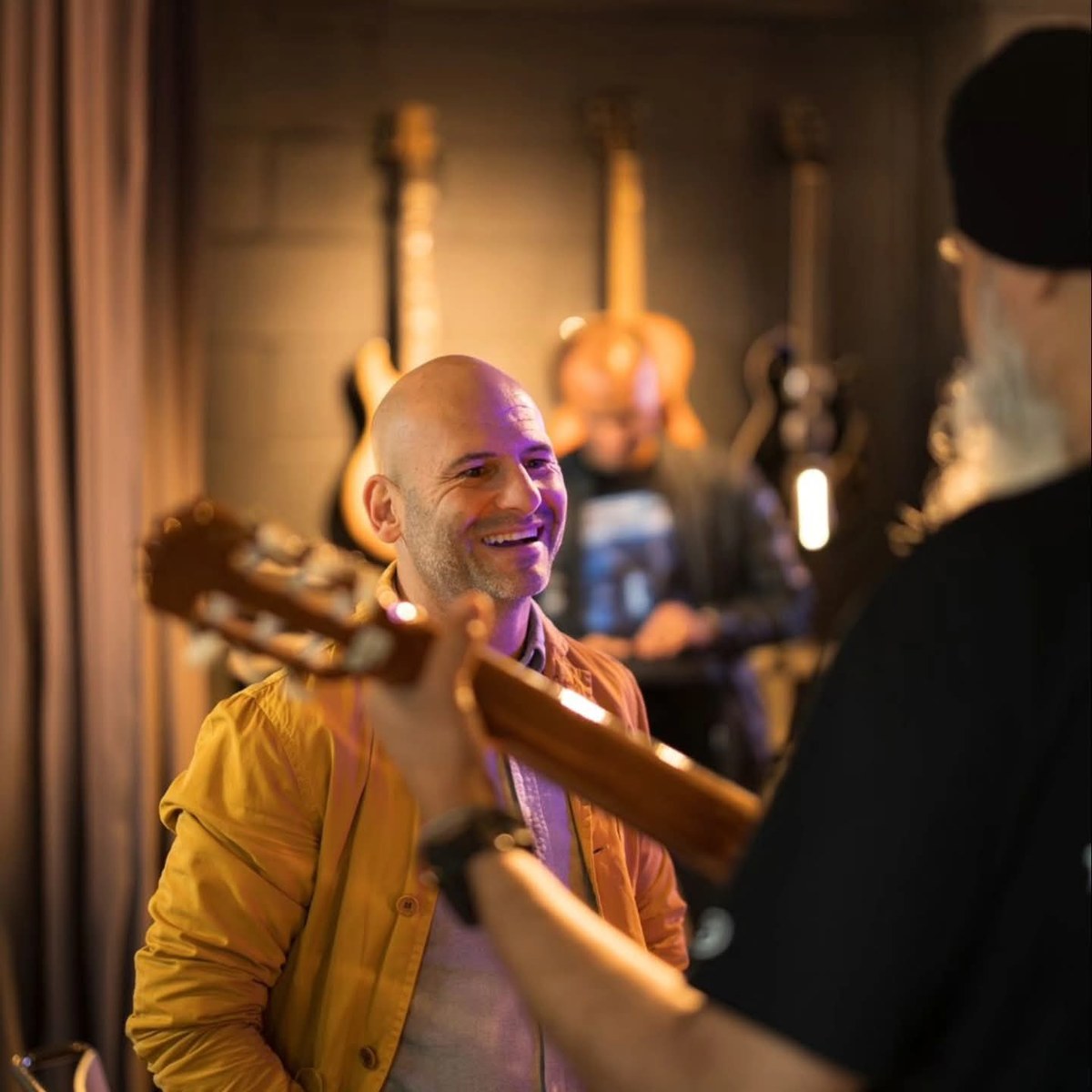 Barry de Jager laughing in conversation with another musician among a wall of guitars