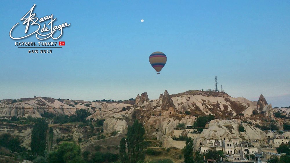 A single striped hot-air balloon and the moon above the fairy-chimney rocks of Cappadocia
