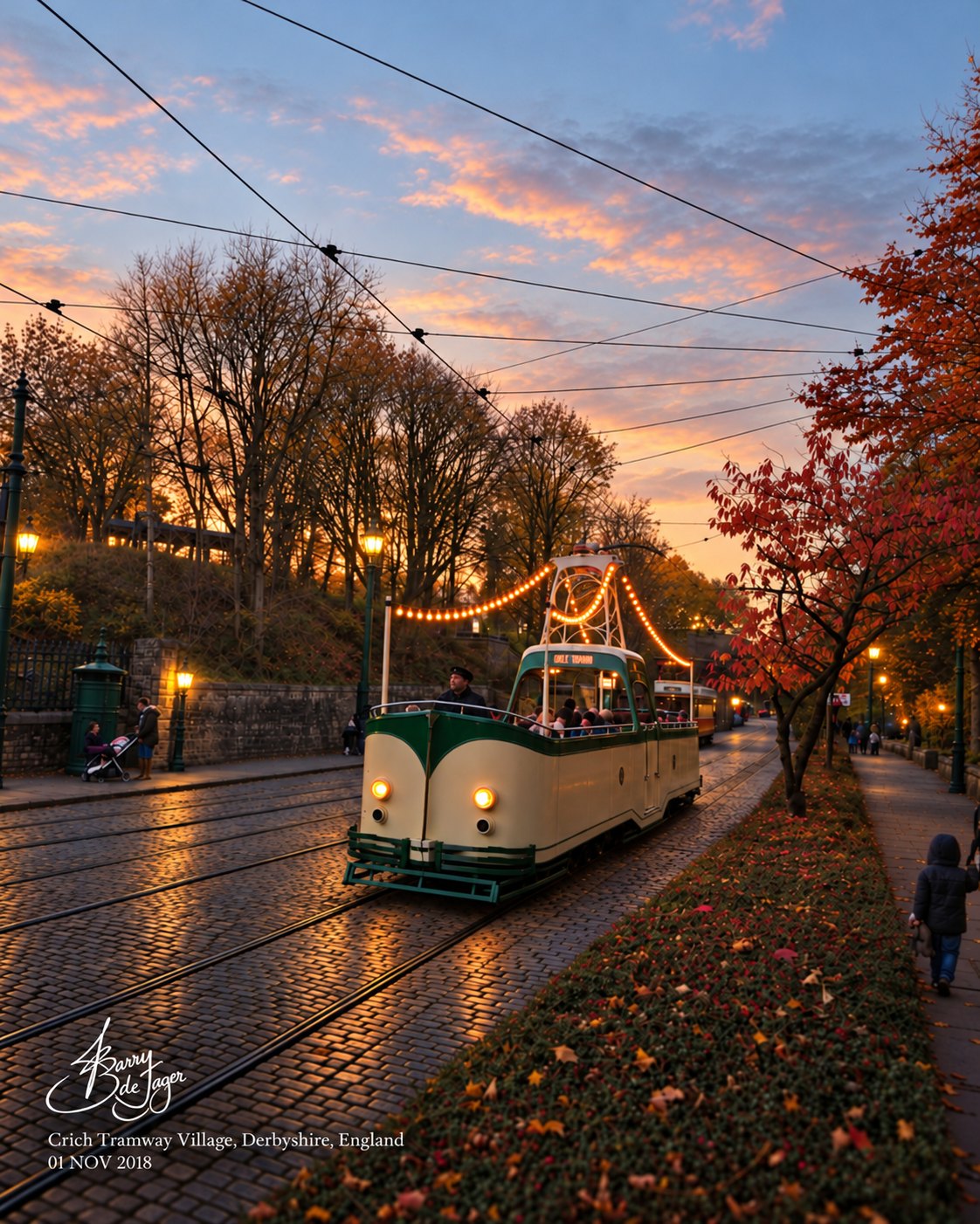 Cream and green tram strung with lights on a cobbled street at dusk, Crich Tramway Village