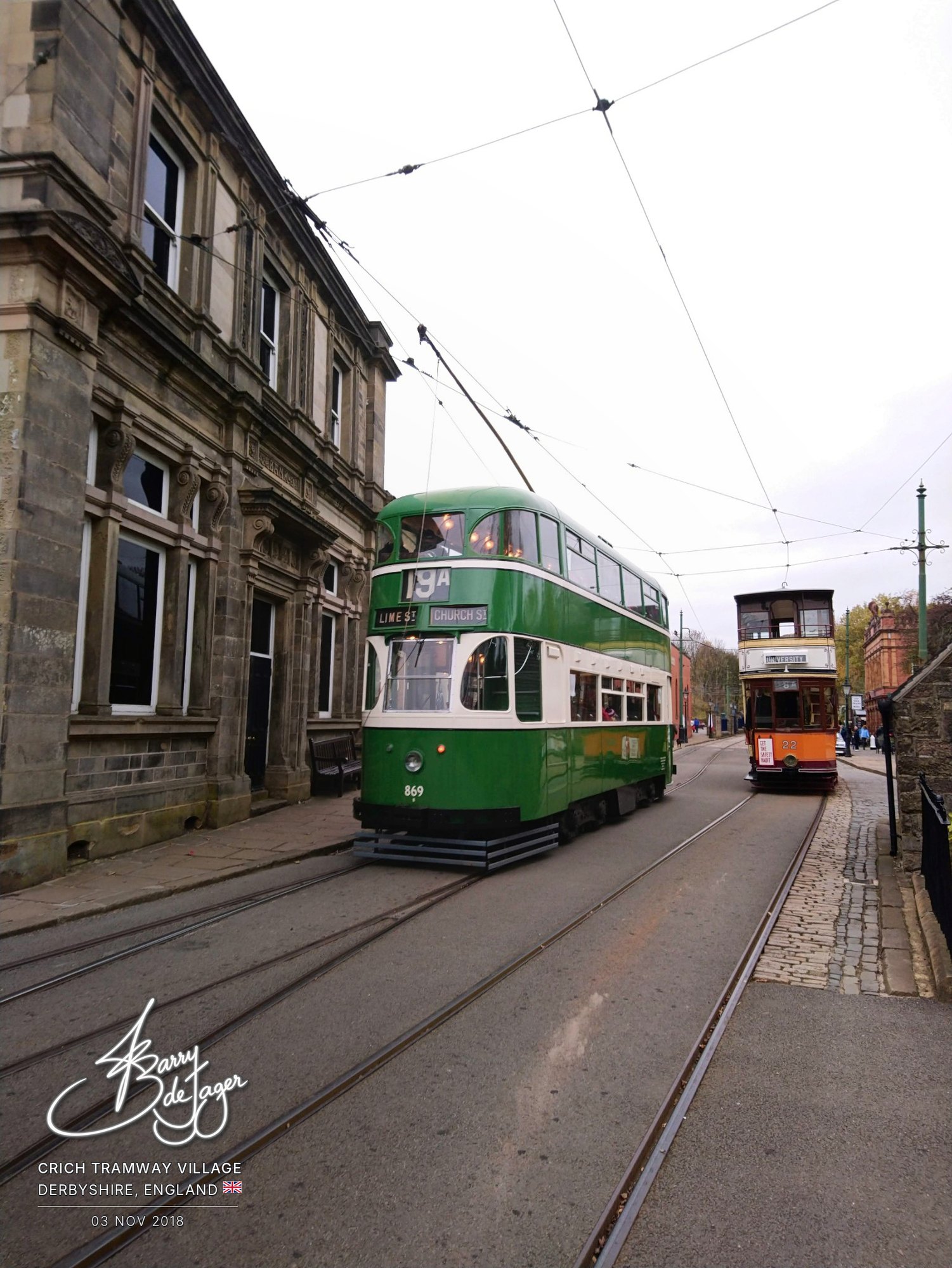 Green double-deck tram 869 beside a stone building, with Glasgow tram 22 behind, at Crich Tramway Village