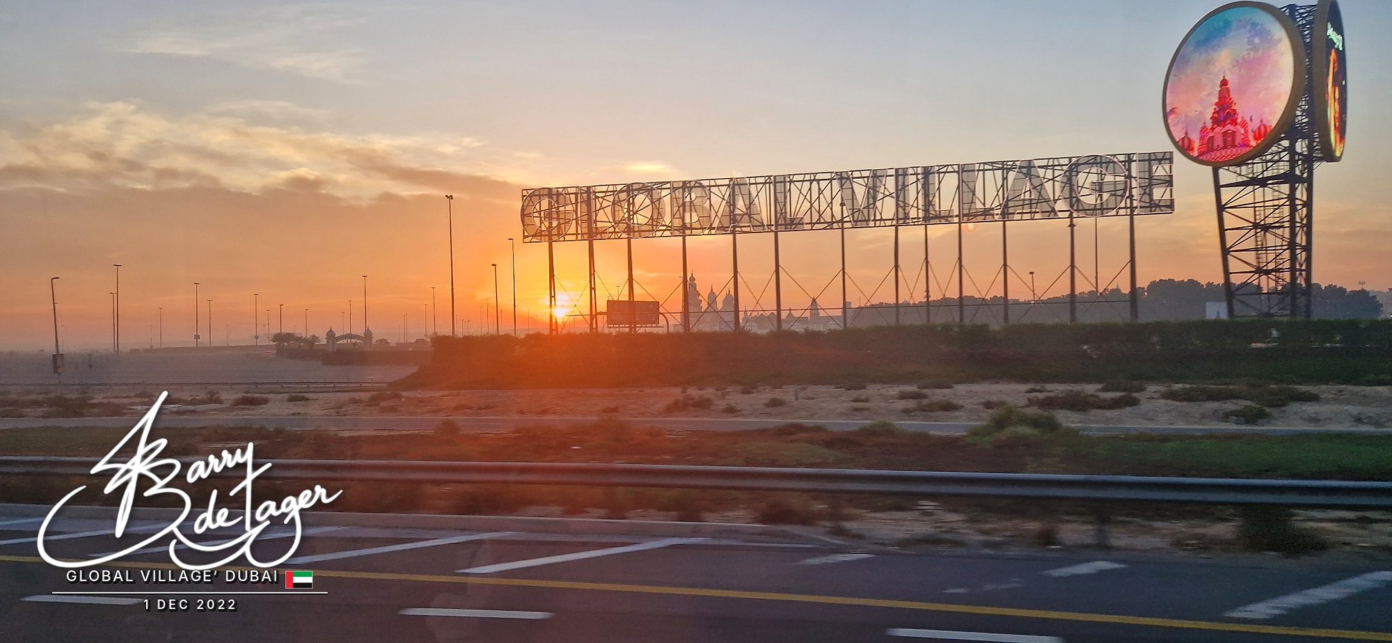 Sun rising behind the giant Global Village sign beside the highway in Dubai