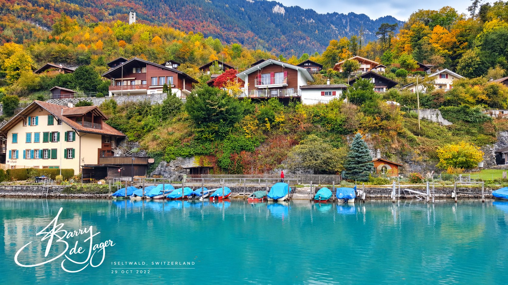 Lakeside chalets and covered boats on turquoise water in autumn at Iseltwald